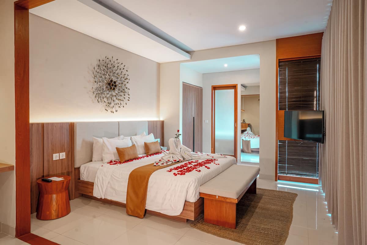 A modern bedroom with a large bed, bedside tables, a TV, and a bathroom visible through an open door.