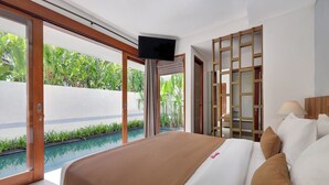 Een hotelkamer met een groot bed, een televisie, uitzicht op een zwembad en een houten scheidingswand.