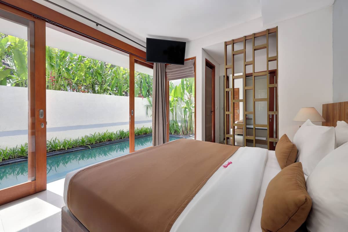A hotel room with a large bed, a television, a view of a swimming pool, and a wooden partition.