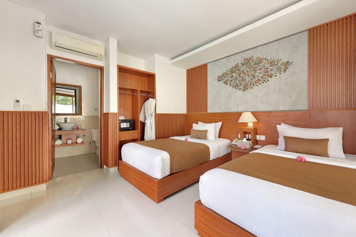 A hotel room with two beds, a bathroom, a wooden wardrobe, and a decorative wall piece.
