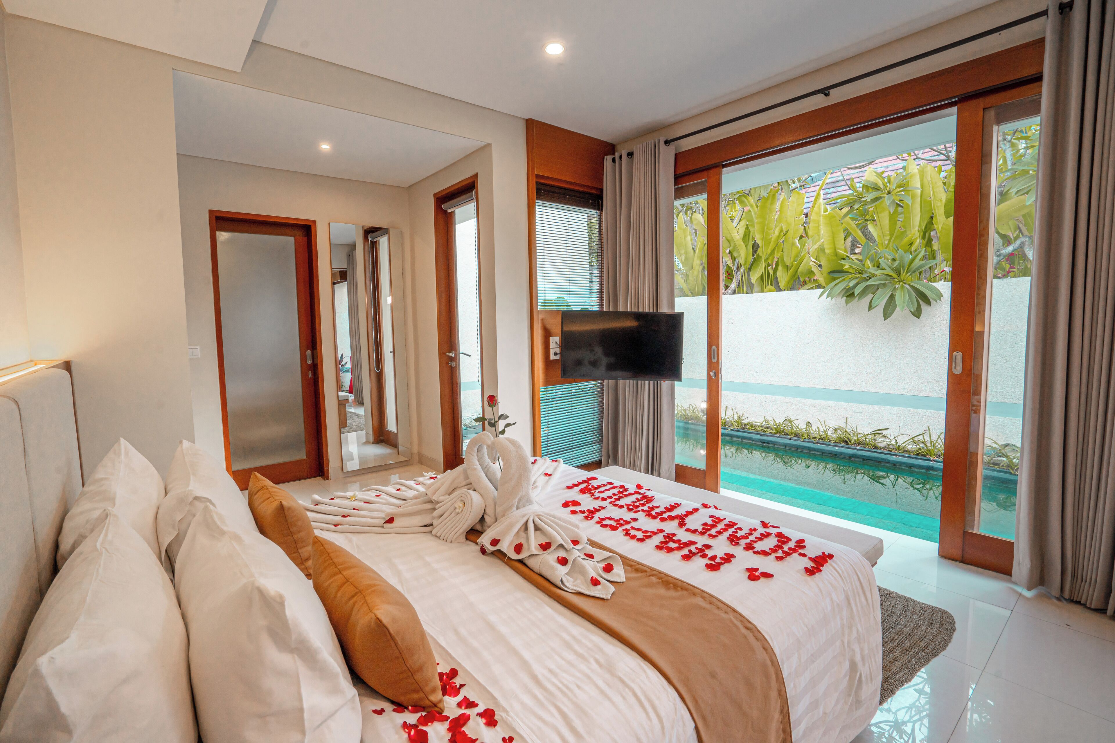A modern hotel room with a large bed, a TV, and a view of a pool.