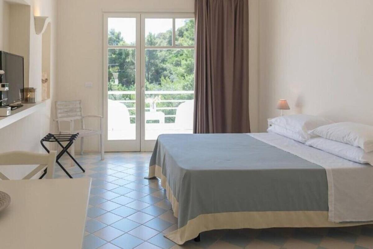 A bedroom with a bed, a desk, a chair, and a window with curtains.