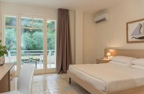 A bedroom with a bed, bedside table, lamp, and a view of a balcony with a table and chairs.