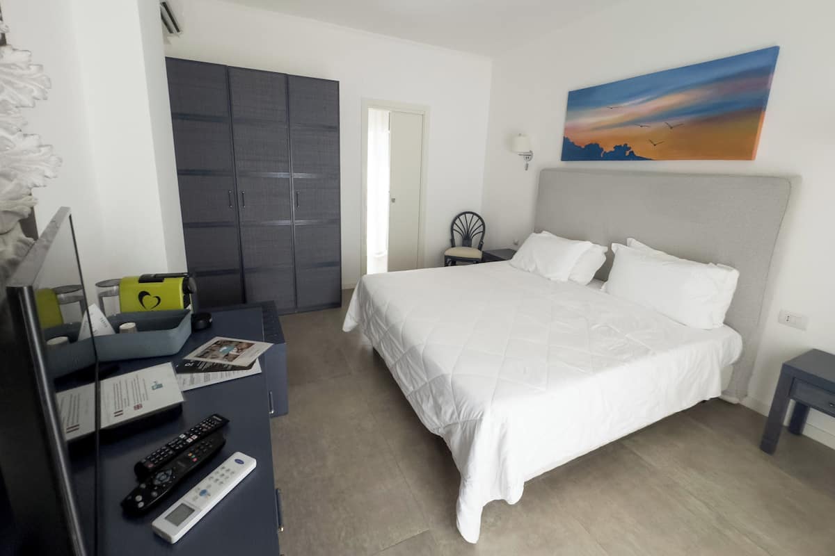 A bedroom with a bed, a desk with a computer, a chair, a wardrobe, and a painting on the wall.