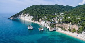 A coastal town with a beach, cliffs, and a mountainous backdrop. - Hotel Baia Dei Faraglioni (Mattinata)