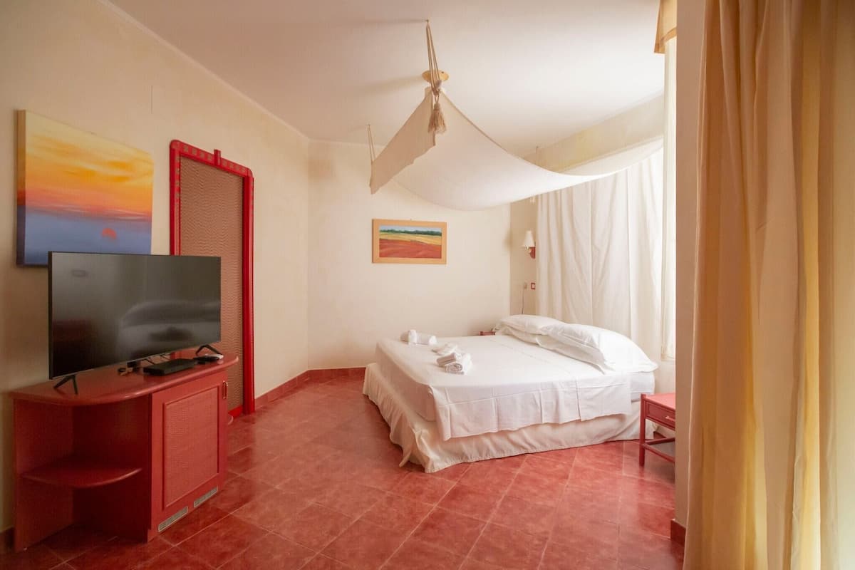 A hotel room with a bed, a television, a painting, and a red cabinet.