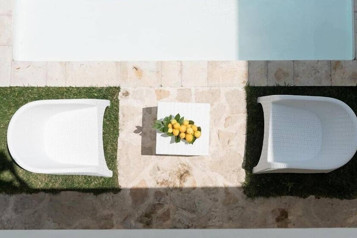 A top-down view of a poolside area with two white lounge chairs and a small table with a bouquet of yellow flowers.