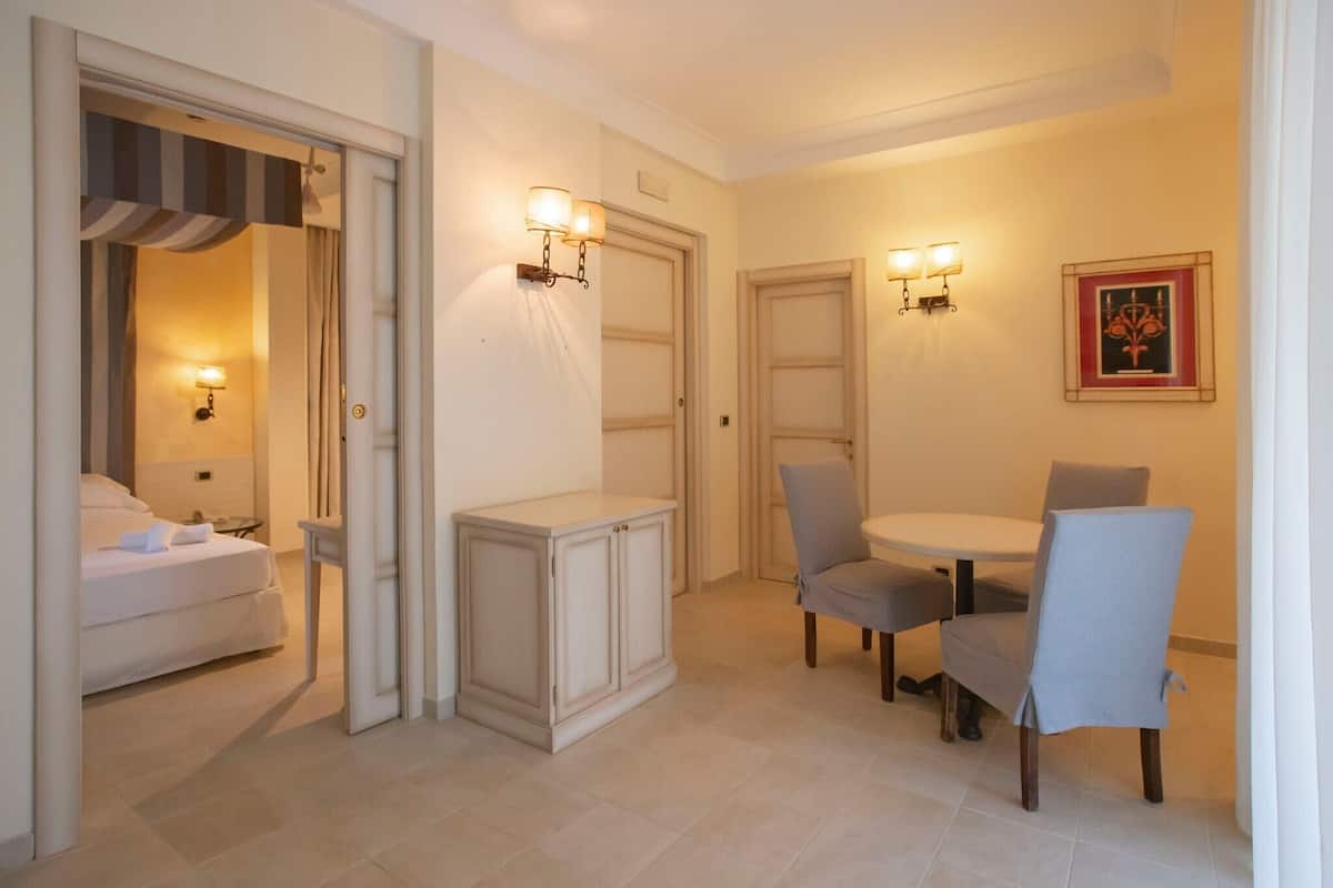 A hotel room with a bed, a small table with two chairs, a cabinet, and two wall-mounted light fixtures.