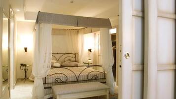 Una cama con dosel y cuatro columnas, un banco al pie, una mesita de noche y un espejo en la pared.