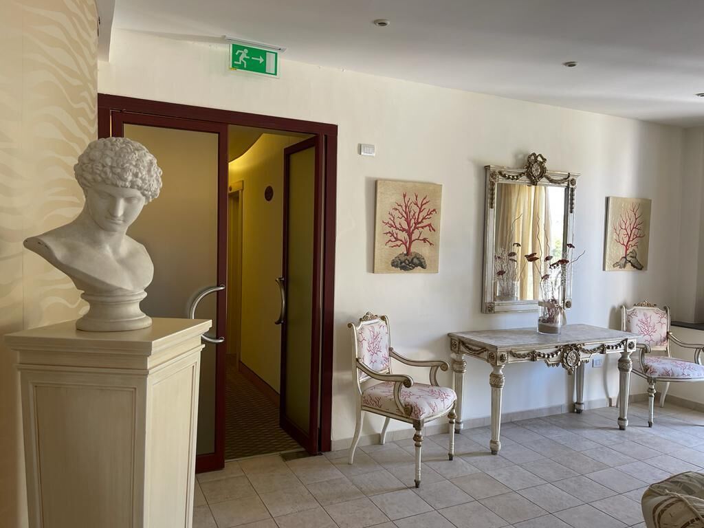 Een hotellobby met een marmeren buste, een spiegel en een tafel met stoelen.