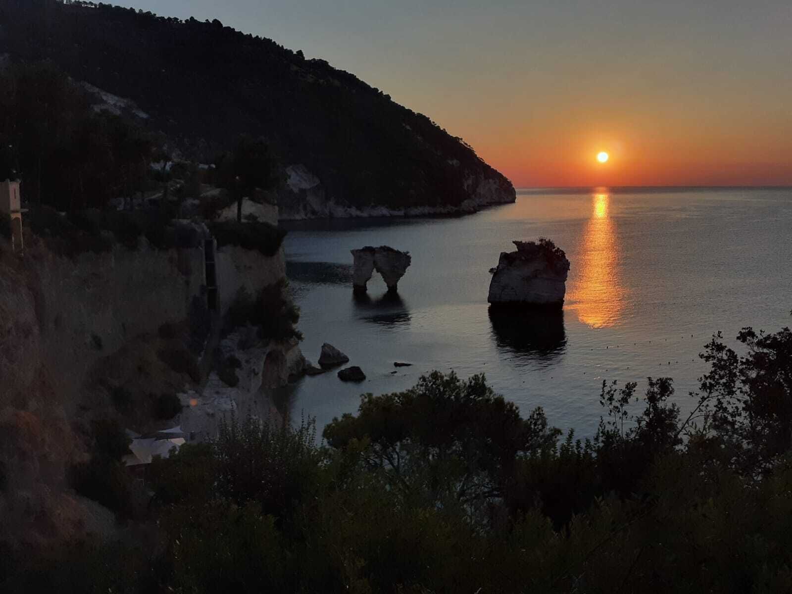 Tramonto sulla costa con formazioni rocciose e mare calmo.