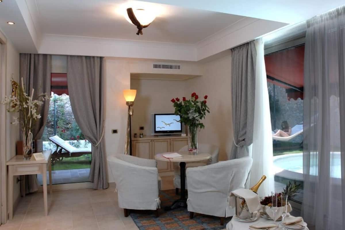 A hotel room with a dining area, a TV, a flower vase, and a view of a pool.