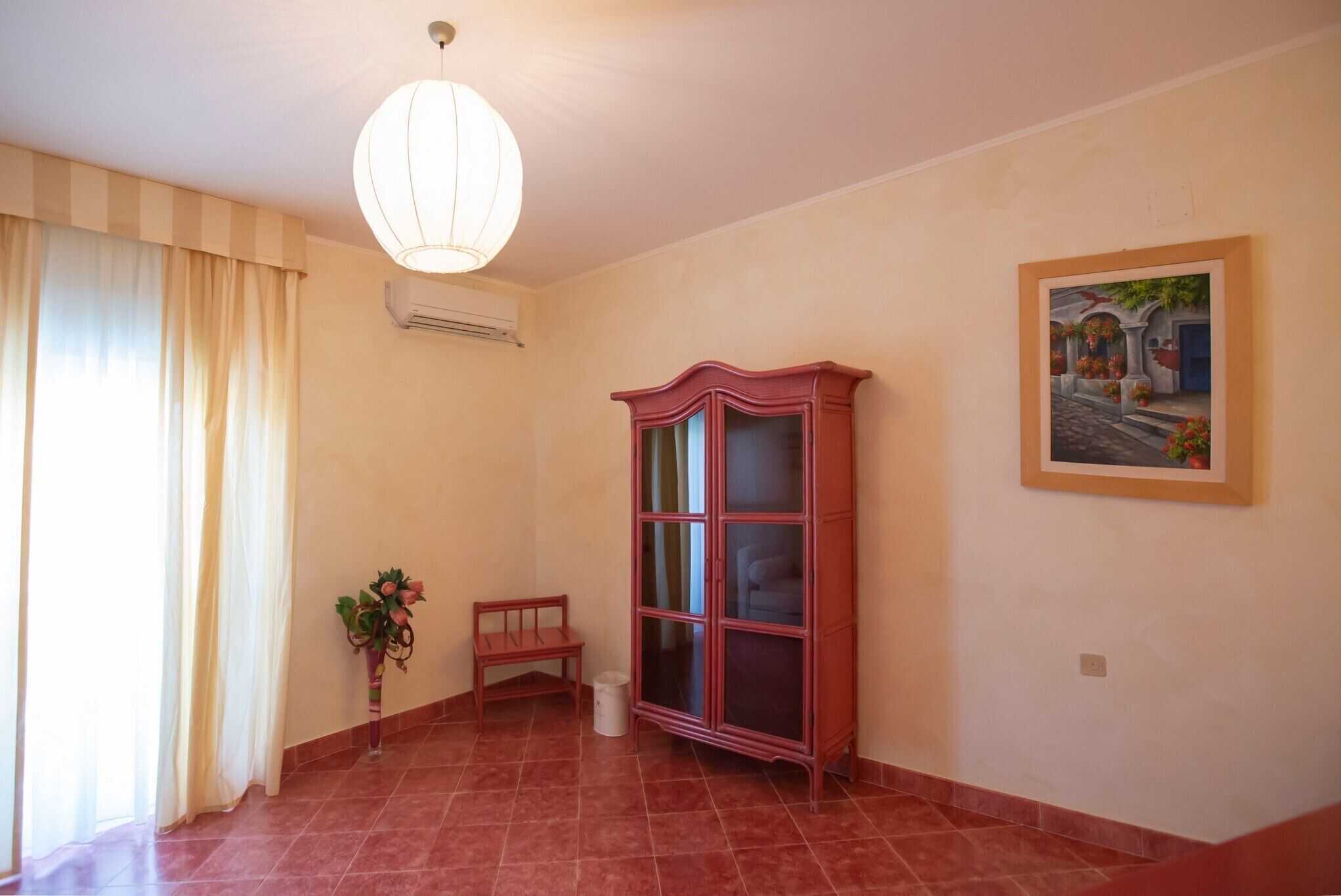 A room with a tiled floor, a wooden bench, a cabinet, a hanging light fixture, and a painting on the wall.