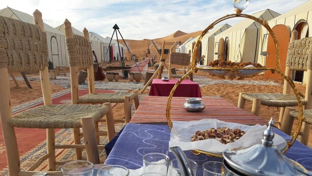 A desert camp with tents, woven furniture, and a table set with glasses and a teapot. - Camp Under Stars - Adults Only (Taouz)