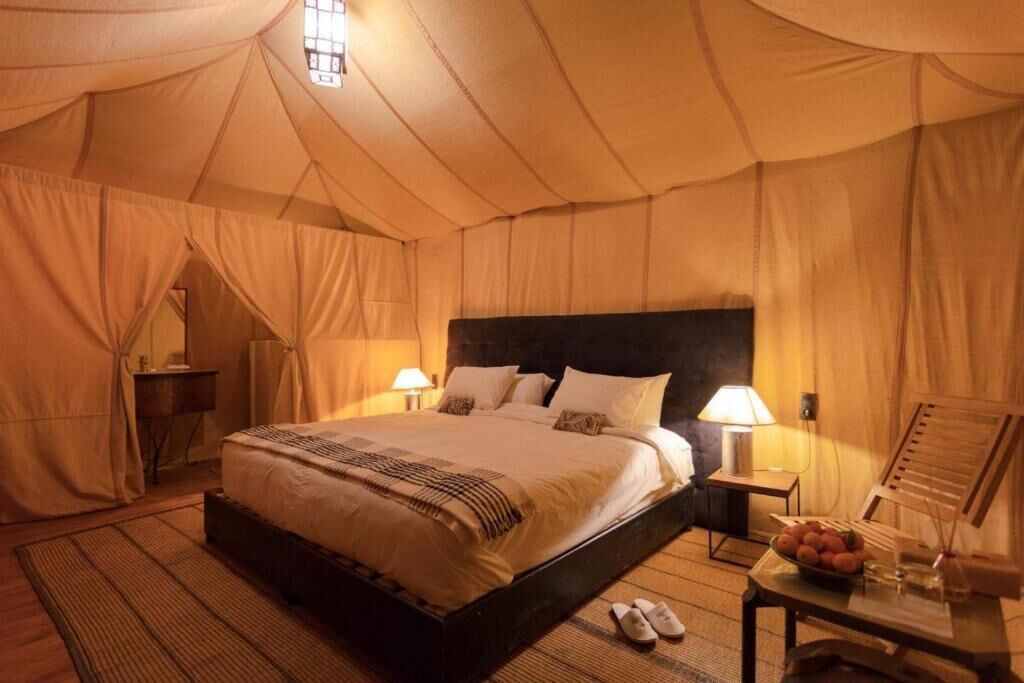 A tent-style bedroom with a bed, bedside lamps, and a small table with a bowl of fruit.