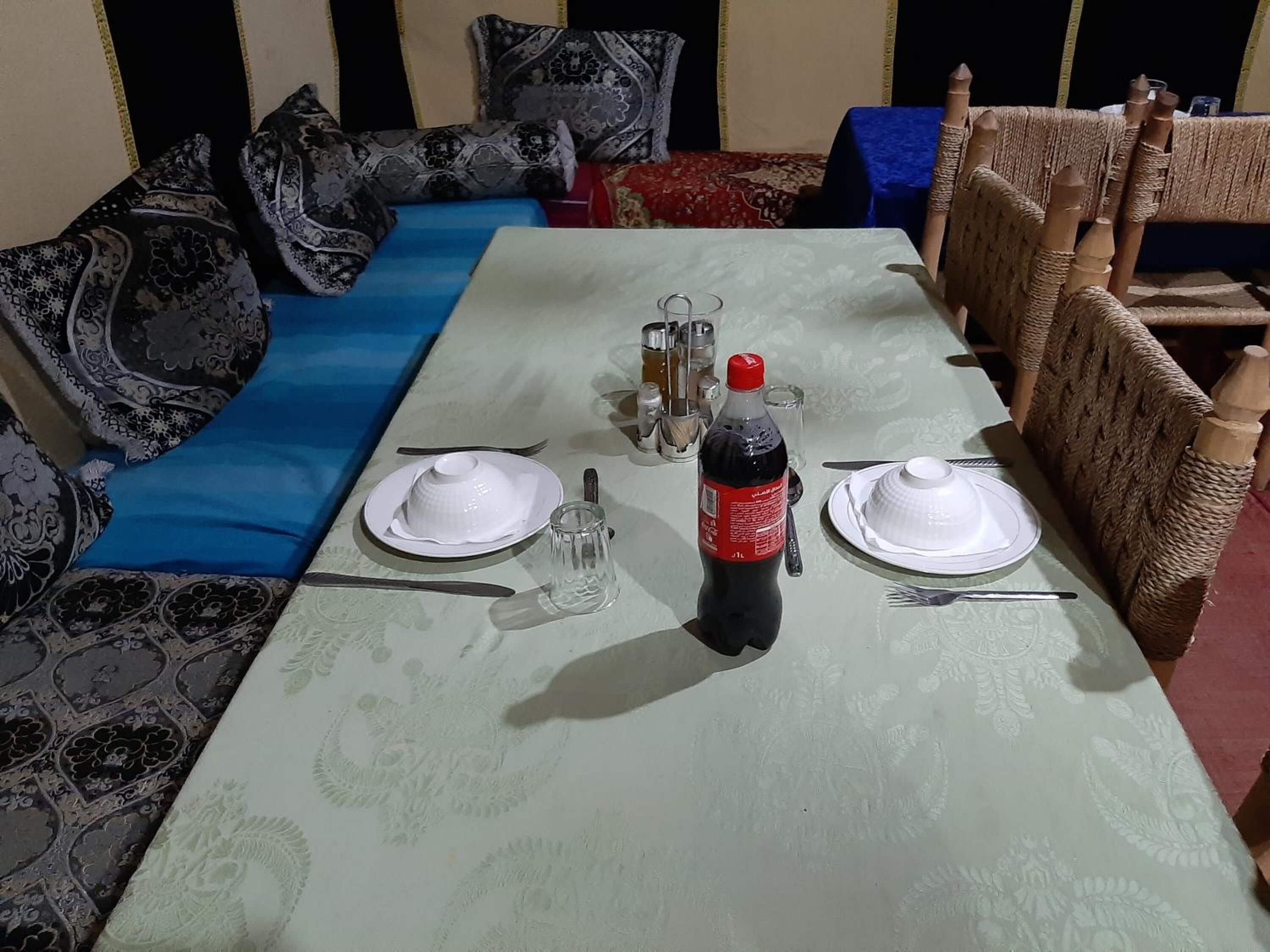 A dining table set with plates, cutlery, a bottle of Coca-Cola, and glasses.