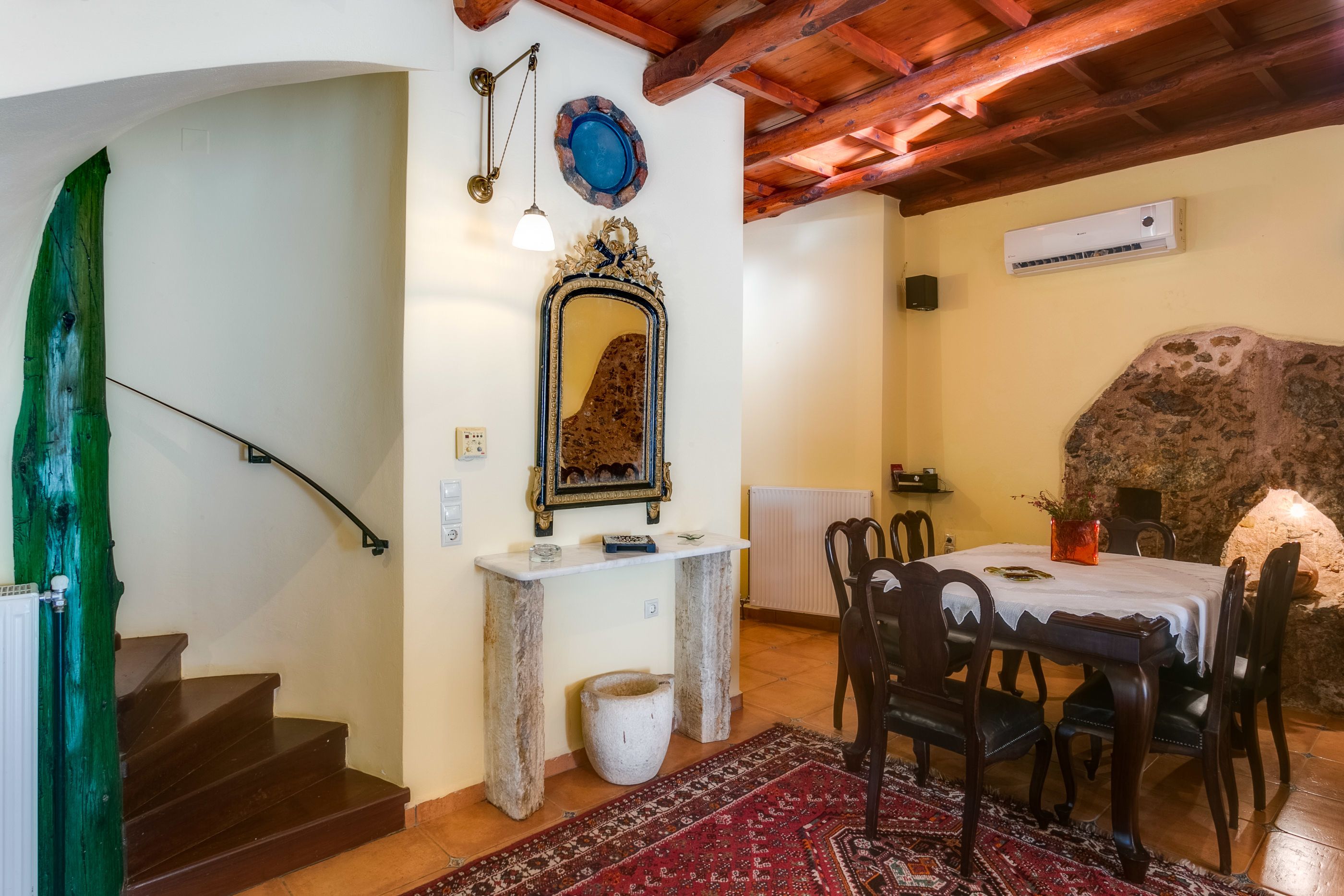 A dining area with a stone wall, a table with chairs, a mirror, and a staircase.