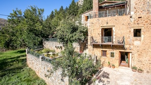 A stone building with a balcony, surrounded by greenery and a stone wall. - Ifigenia Theriso Village (Chania)