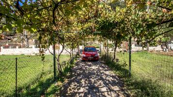 A red car parked under a vine-covered archway on a stone path.