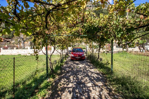 Une voiture rouge était garée sous une arche recouverte de vigne, le long d’un chemin de pierres.