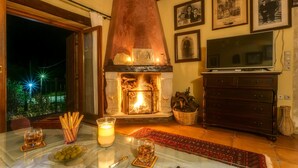 A cozy living room with a fireplace, a television, and a dining area with a table set for two. - Ifigenia Theriso Village (Chania)