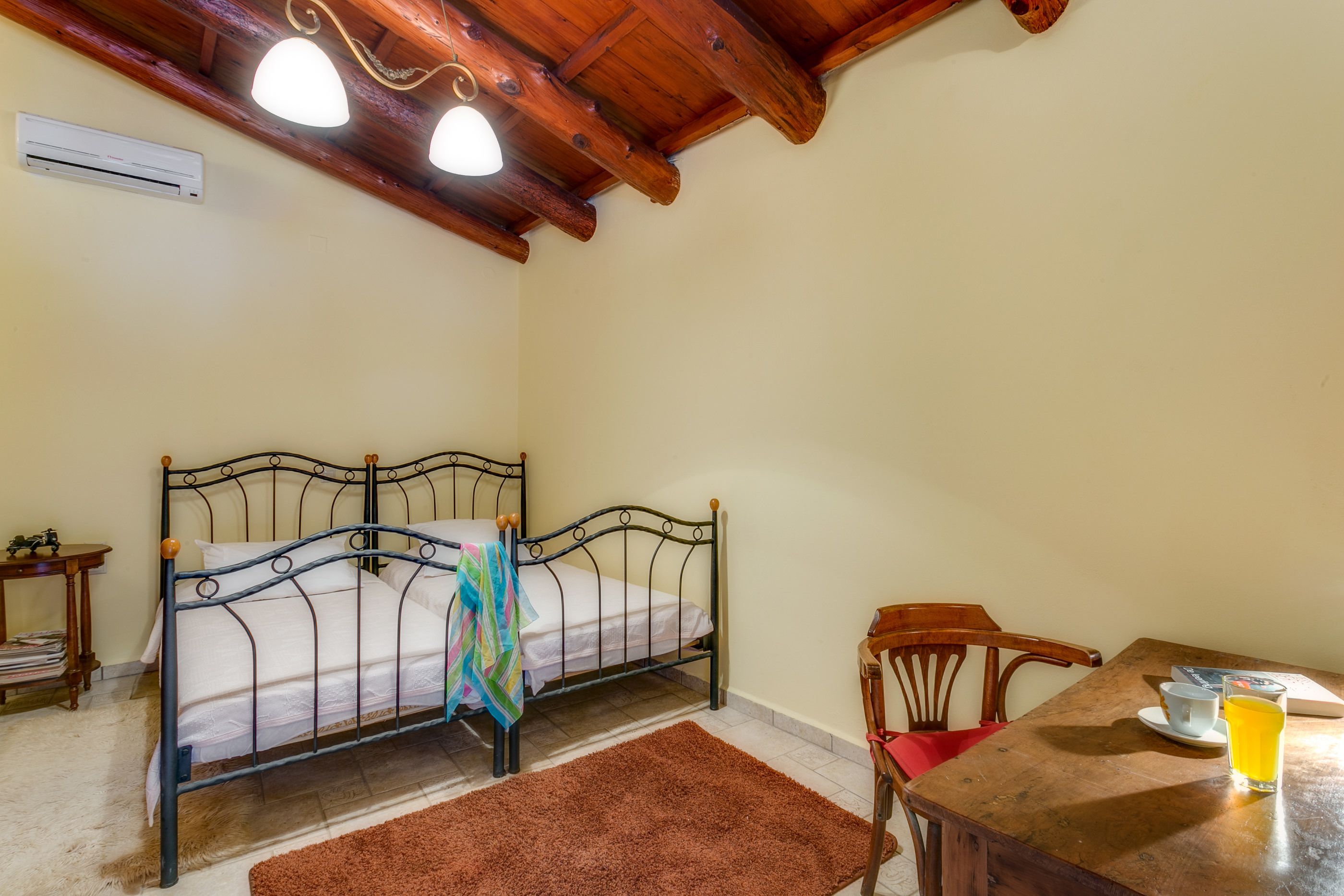 A bedroom with a metal bed frame, a wooden table with a chair, and a small bedside table.