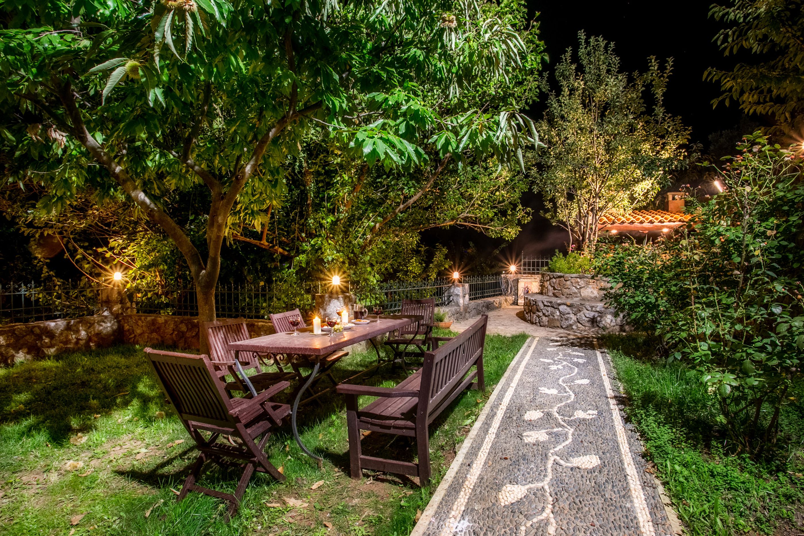 An outdoor dining area with a table and benches, surrounded by lush greenery and a stone wall.