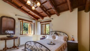 A bedroom with a wooden ceiling, a bed with a metal frame, a bedside table with a lamp, and a window with curtains. - Ifigenia Theriso Village (Chania)