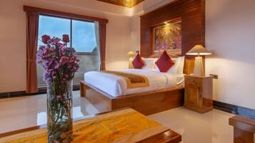 A hotel room with a bed, a wooden headboard, a nightstand, a lamp, a vase with flowers, and a window with curtains.