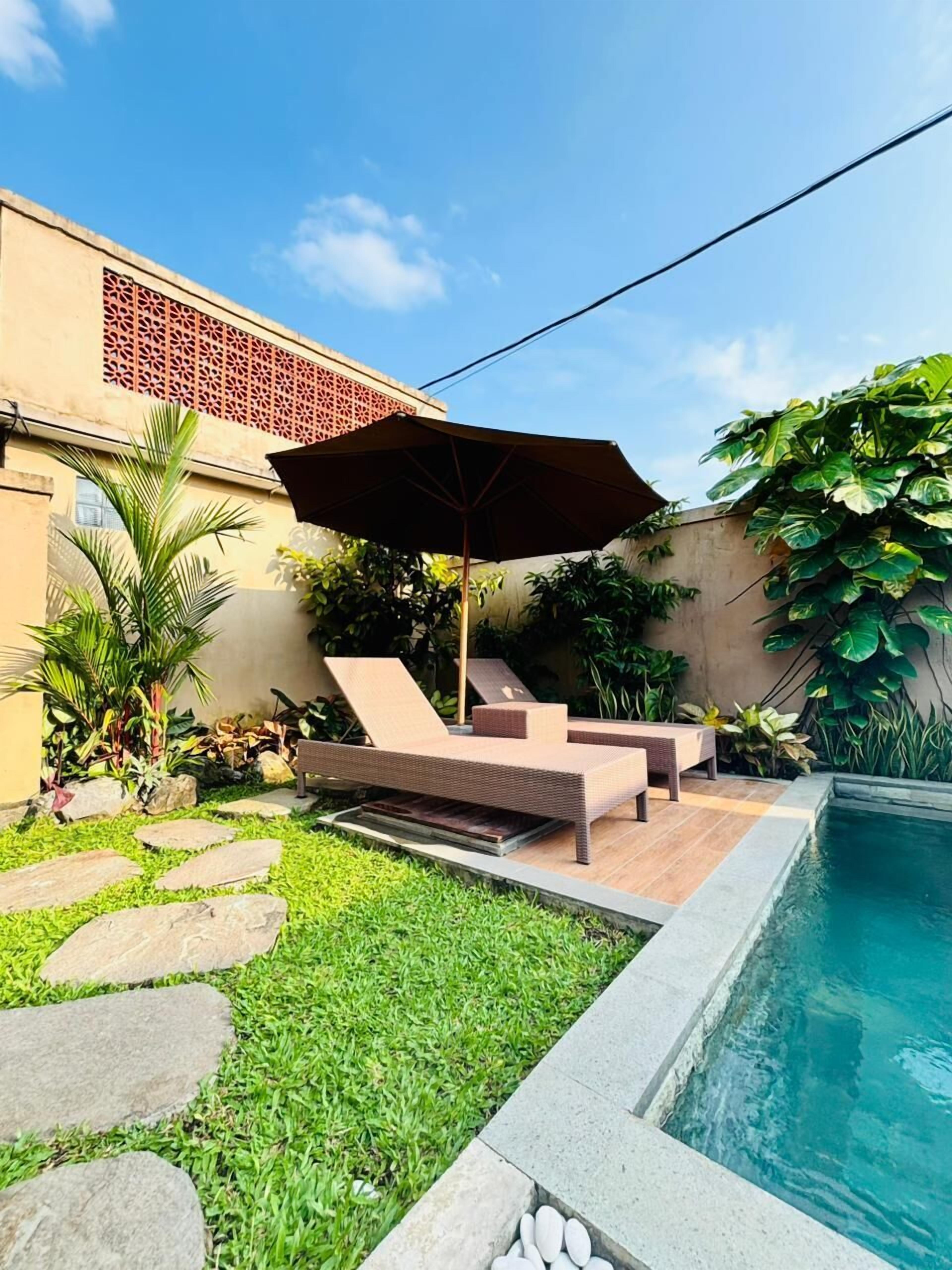 Un patio trasero con piscina, un área de descanso con una sombrilla grande y un sendero de piedra.