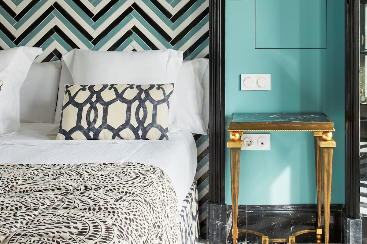 Une chambre à coucher avec un lit, des coussins à motifs, une table de chevet et un mur orné d’un motif en chevrons.