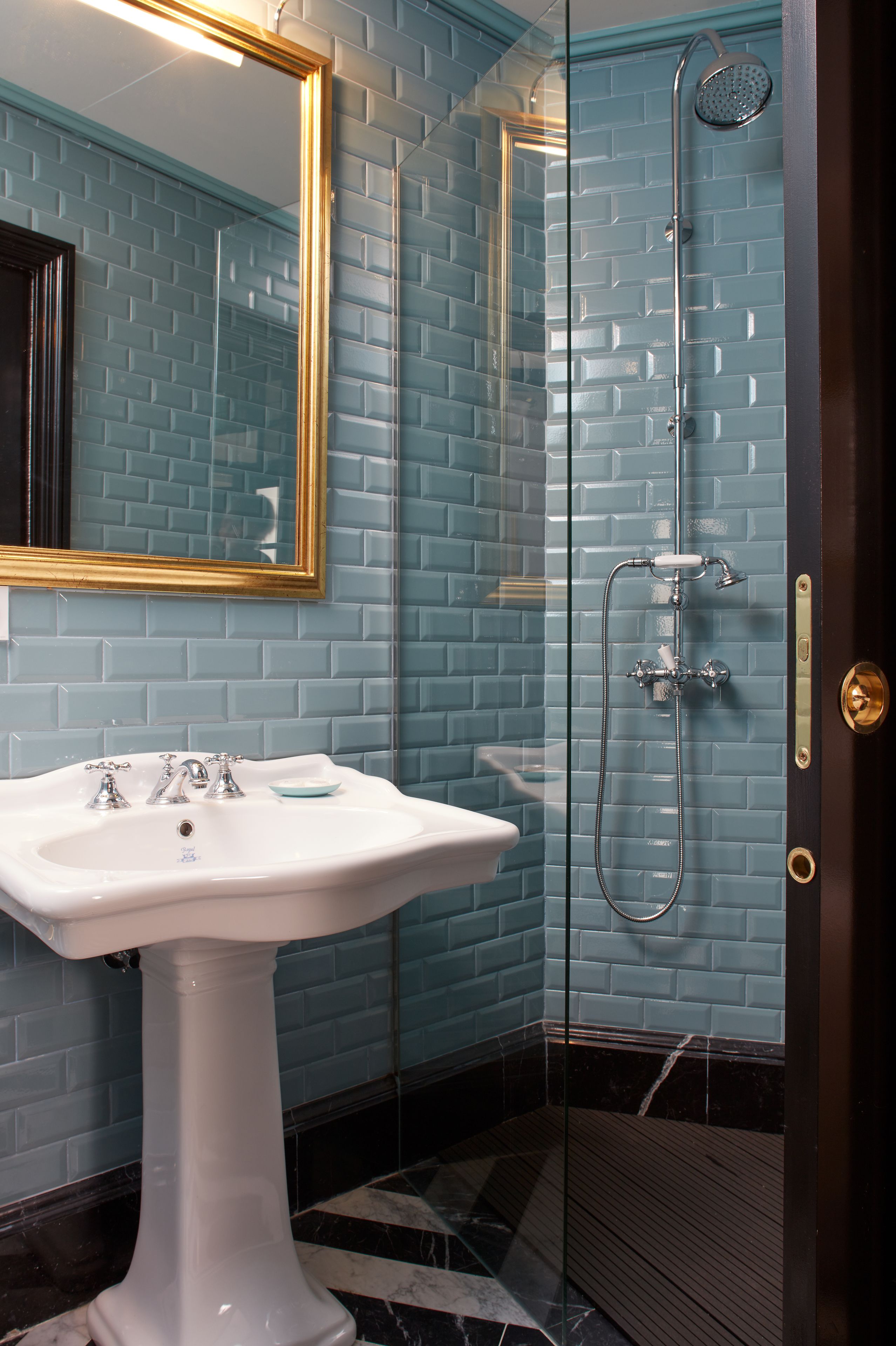 A bathroom with a white pedestal sink, a glass-enclosed shower, and a blue-tiled wall.