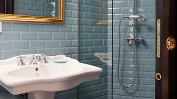 A bathroom with a white pedestal sink, a glass-enclosed shower, and a blue-tiled wall.