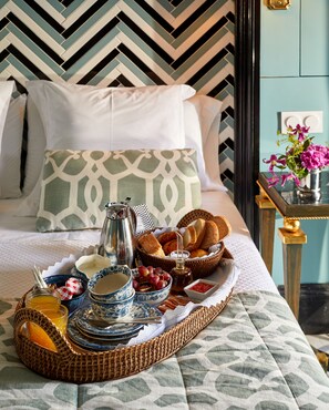 Un plateau de petit-déjeuner soigneusement préparé, avec du pain, des viennoiseries et des boissons, posé sur un lit agrémenté de draps et d’oreillers à motifs.