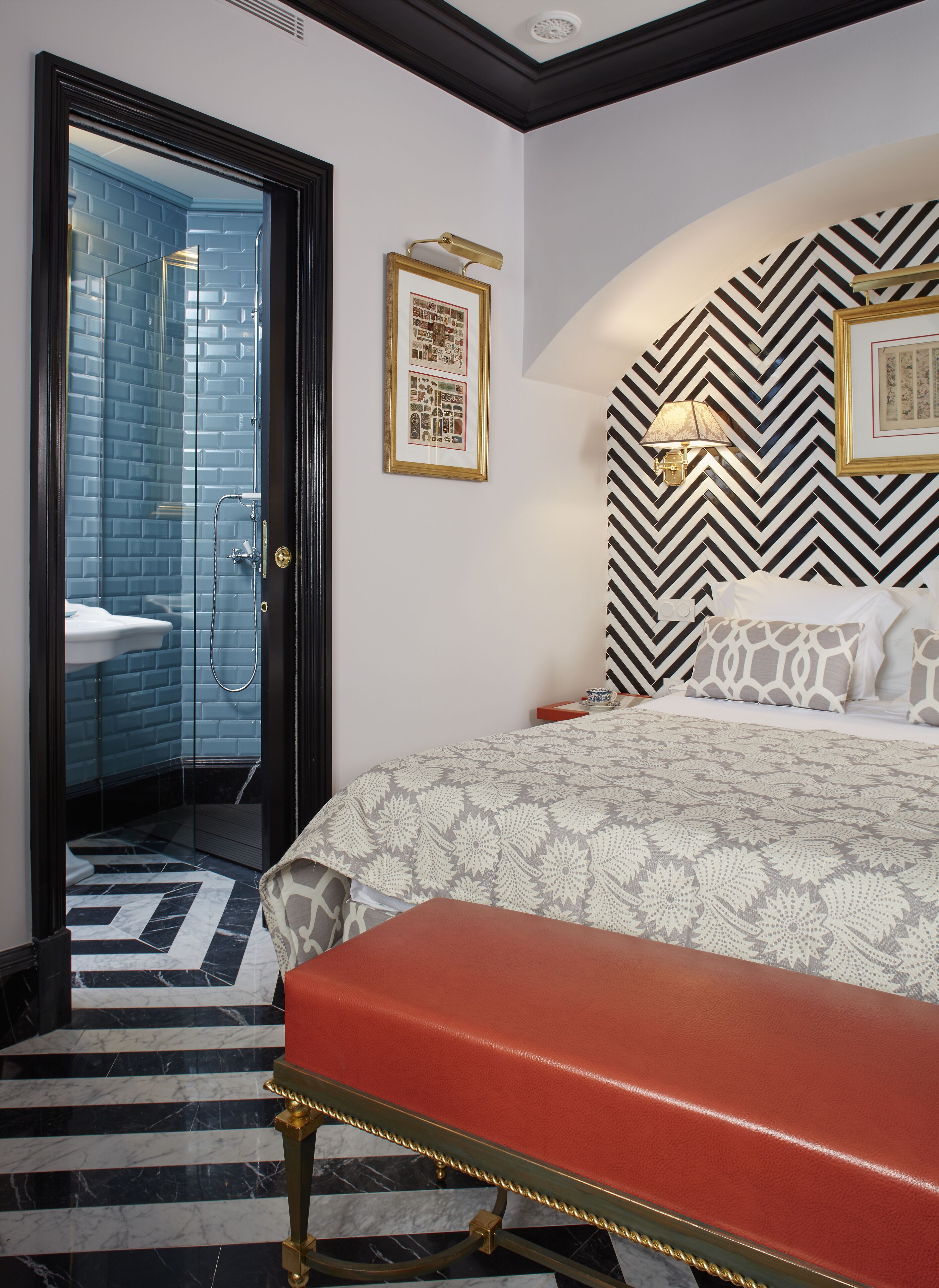 A hotel room with a bed, a bench, a shower area, and a patterned wall.