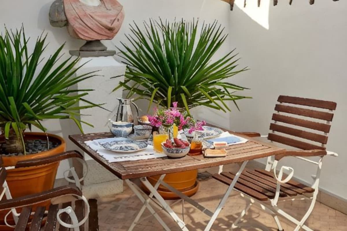Une terrasse extérieure avec une table en bois, deux chaises et des plantes en pot.