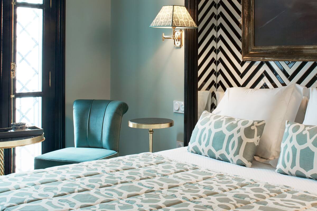Une chambre d’hôtel avec un lit, une chaise, une petite table et une lampe.