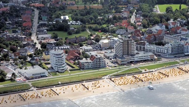 Vista aerea di una località costiera con spiaggia, edifici e una strada.