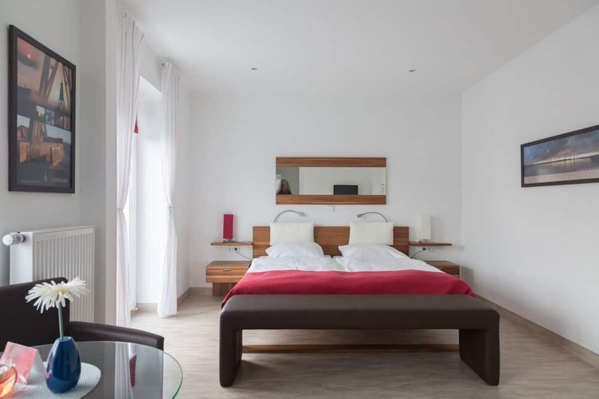 A modern bedroom with a large bed, a bedside table, a mirror, and a chair.