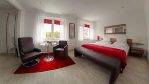 Una camera d'albergo moderna con un letto, due poltrone, un tavolino e un tappeto rosso.