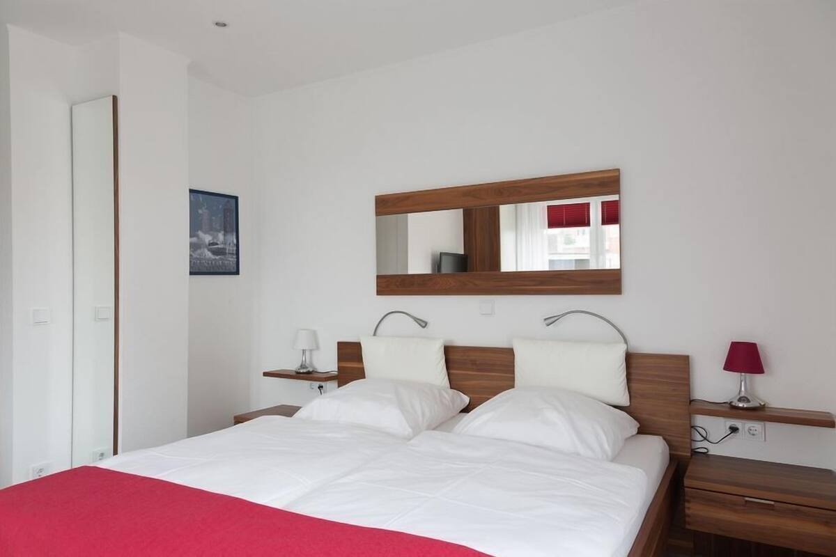 A hotel room with a large bed, a wooden headboard, a bedside table with a lamp, and a mirror on the wall.