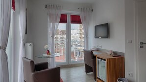 Una camera d'albergo moderna con un balcone, un piccolo tavolo da pranzo, un divano e una TV a parete.