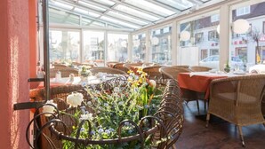 Un ristorante con mobili in vimini, pareti vetrate e un'elegante composizione floreale.