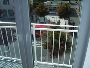 A balcony with a metal railing, a view of a street with trees and a building, and a clear sky. - Hotel Christiansen (Cuxhaven)