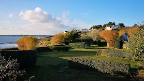 Une propriété située sur la côte, dotée d’un jardin bien entretenu, d’un sentier menant à la mer et de maisons adossées à une colline.