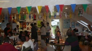 Un espace repas avec des tables et des chaises, des personnes qui déjeunent ou dînent, et des drapeaux triangulaires aux couleurs vives suspendus au plafond.