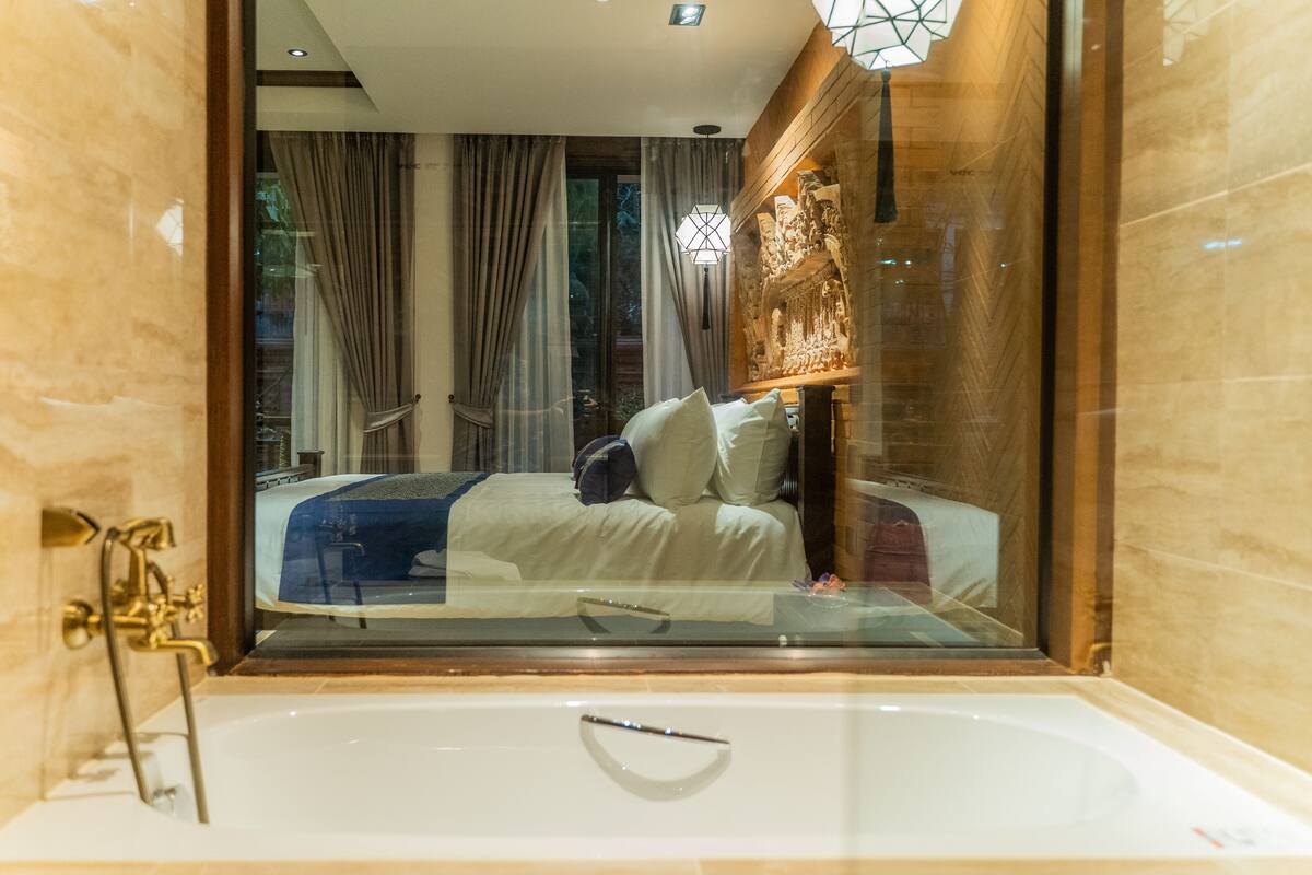 Une salle de bain moderne dotée d’une douche à parois de verre, d’une baignoire et d’une chambre à coucher ouverte, avec un lit et des rideaux.