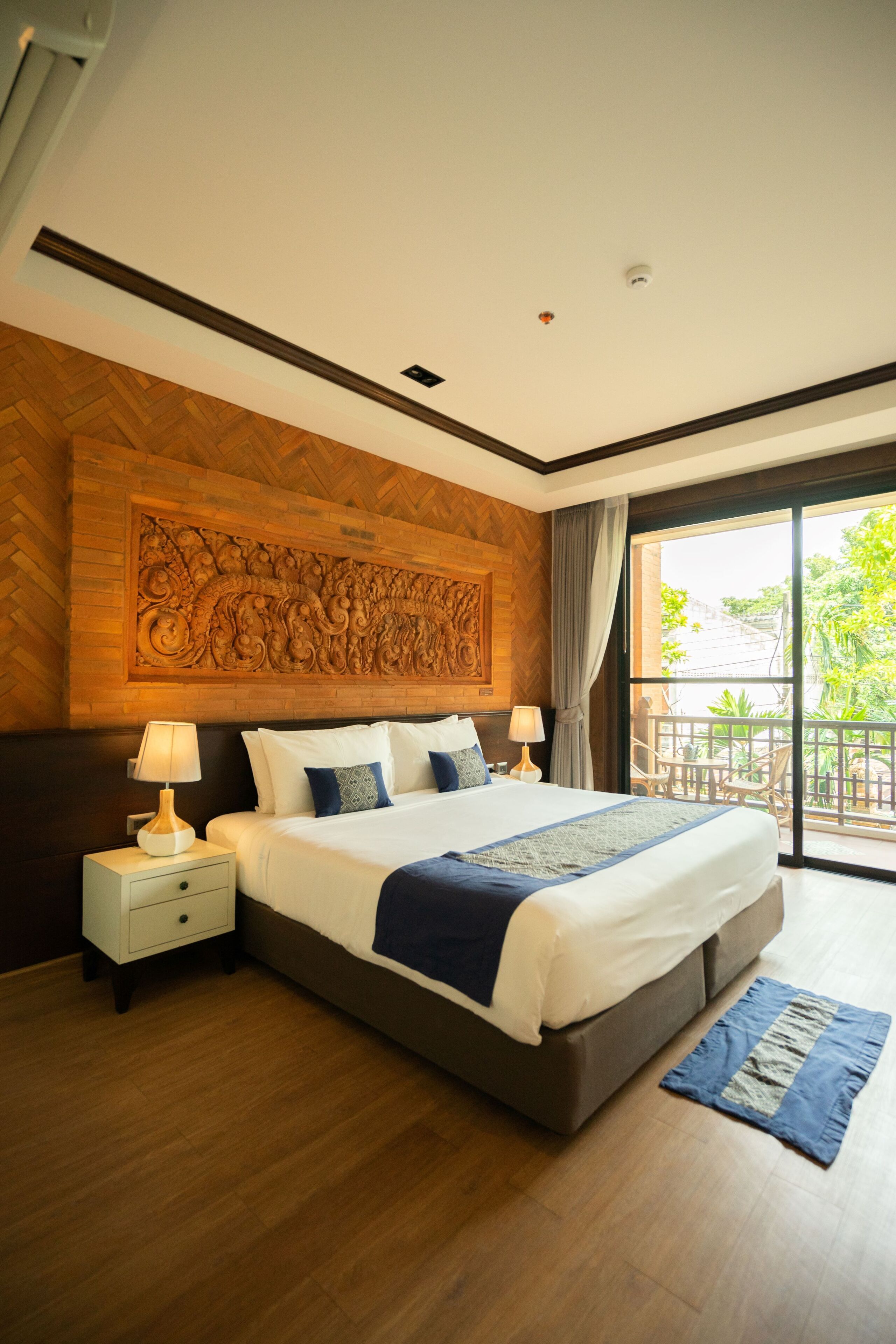 A modern hotel room with a large bed, wooden headboard, and a balcony with a view.