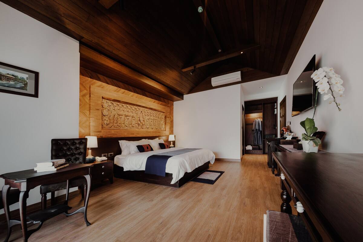 Une chambre d’hôtel moderne avec un plafond en bois, un grand lit avec une literie blanche, un bureau avec une lampe et une plante en pot.