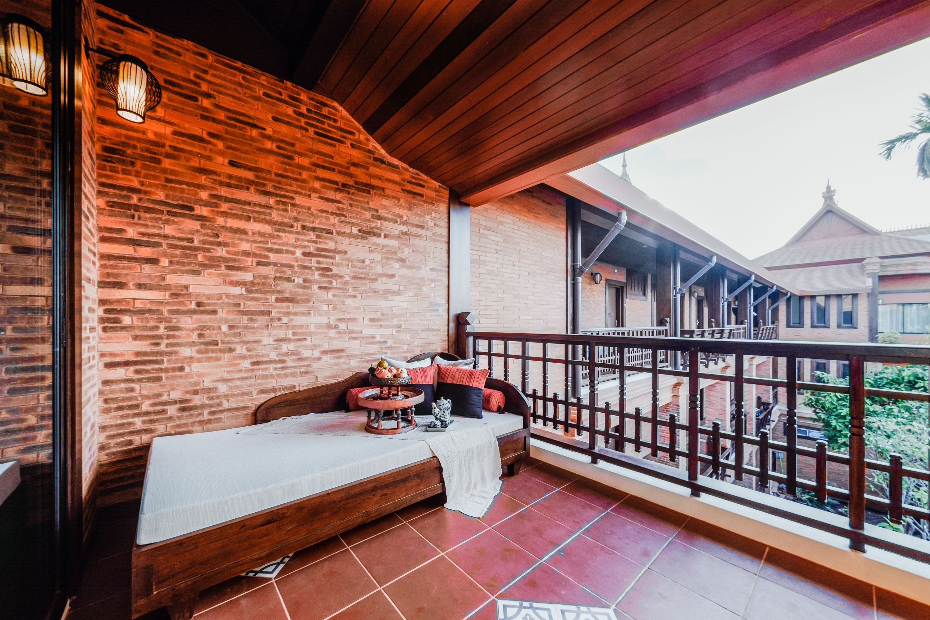 Een balkon met een houten bankje, een bakstenen muur en uitzicht op traditionele gebouwen.